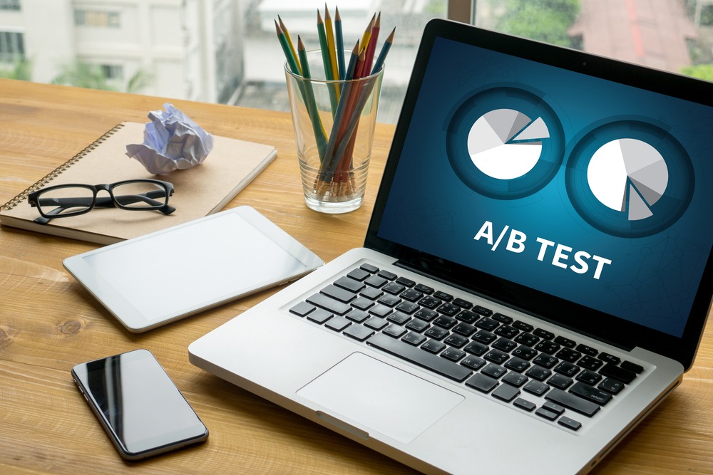 Computer shows an a/b test on a desk with pencil, glasses and phone in the background.